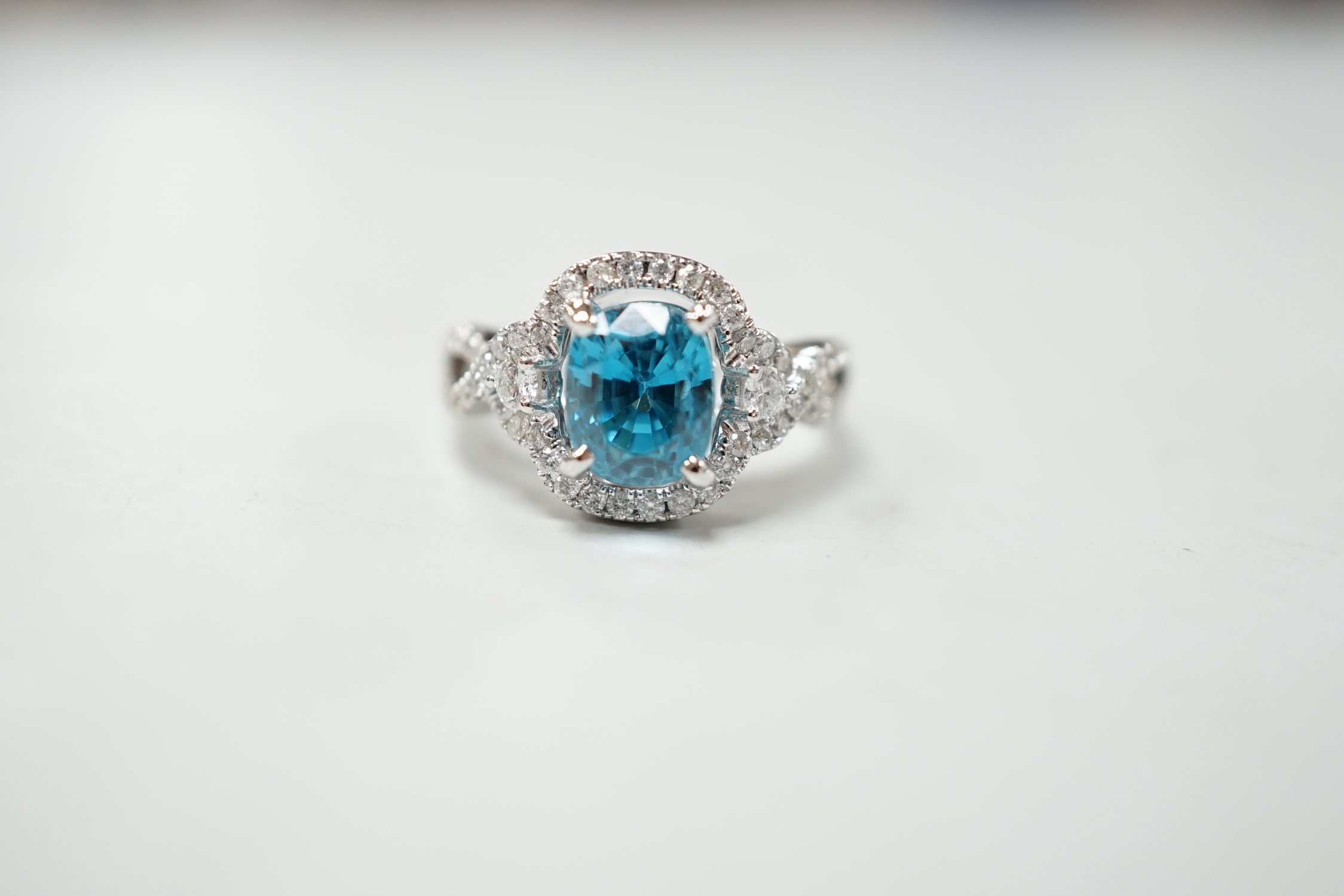 A modern 14k white metal, cushion cut blue zircon and diamond chip set cluster dress ring, with diamond chip set shoulders, size O, gross weight 6.8 grams.